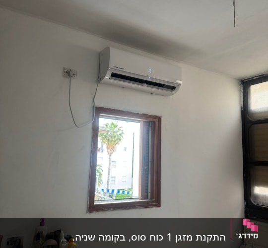 מזגן מותקן על קיר לבן מעל חלון פתוח